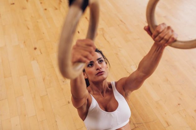 Determined young woman at gym. Muscular female athlete working out using gymnastic rings.