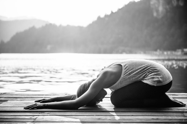 Young woman doing yoga by the lake, relaxing in childs pose. Black and white image
