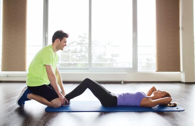 fitness, sport, training, teamwork and people concept - woman with personal trainer doing sit ups in gym