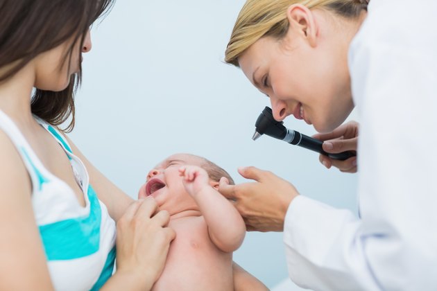 Mother holding a baby in an examination room with a doctor using an otoscope