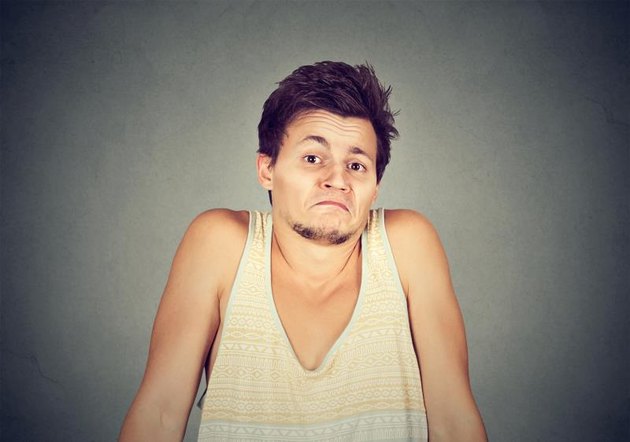Ignorance and arrogance. Closeup portrait young man shrugging shoulders who cares so what I don't know gesture isolated on gray wall background. Human body language. Whatever attitude reaction