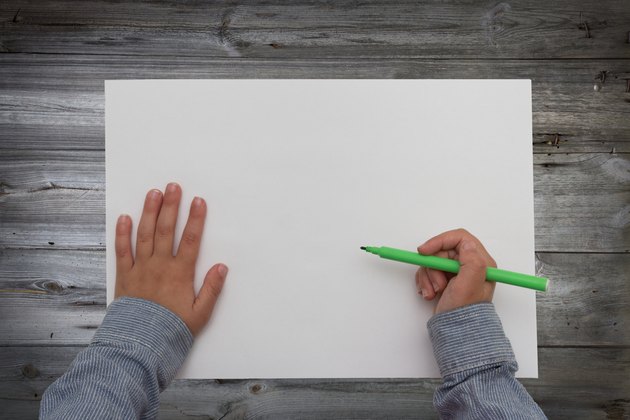 child holding pen over blank sheet of paper. kids hands