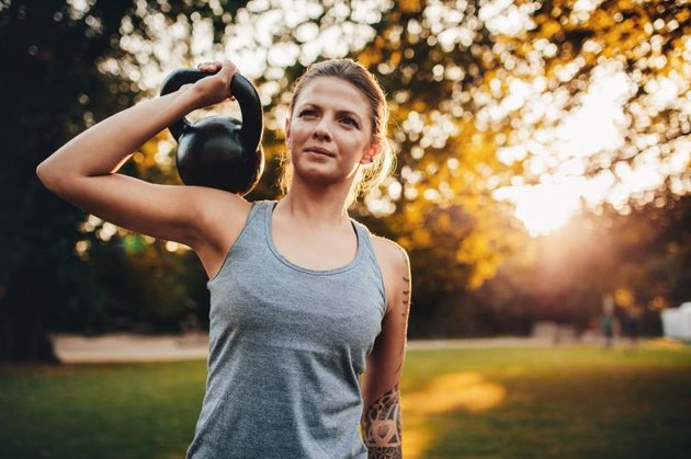 Portrait of fit young woman with kettlebell weights in the park. Fitness woman training with weights in park.
