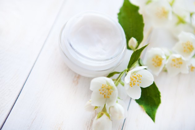 Pot of beauty cream with flower on white wooden table