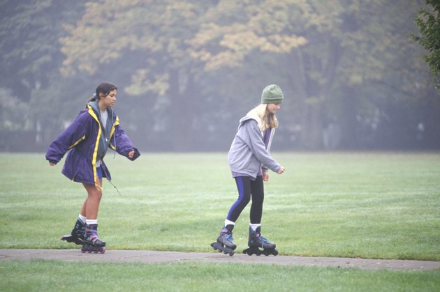Two teenage girls (13-14) in-line skating in park, (Side view)