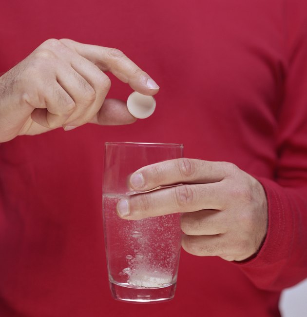Man dropping second tablet into fizzing glass of water, close-up
