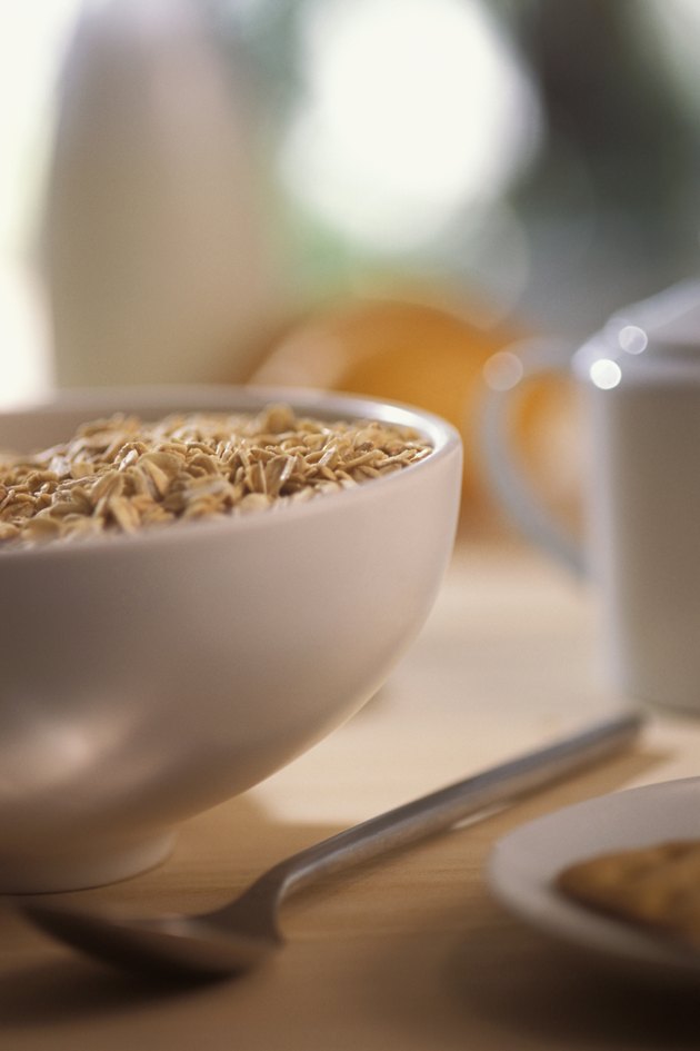 Bowl of cereal with spoon and edge of plate with pastry on it, close-up