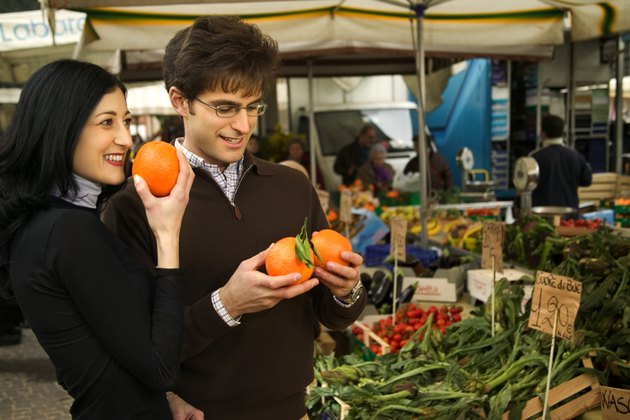 A couple shops for fruit, smelling oranges in an outdoor fresh market in Italy.