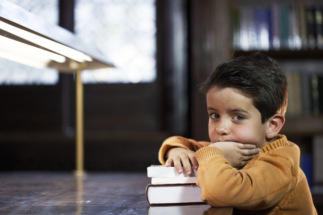 Boy (5-7) sitting at library table, resting arm on books, portrait