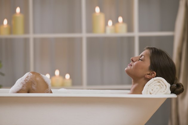 Content woman lying in bathtub with candles