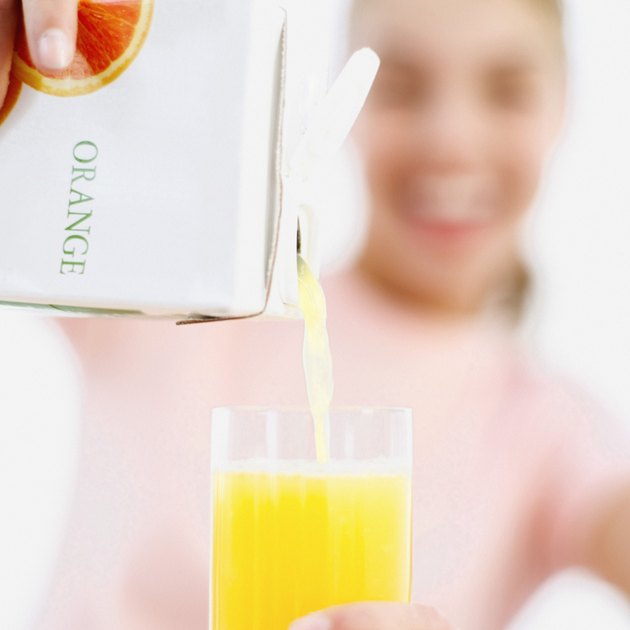 Close-up of a young woman's hands pouring juice from a carton into a glass (blurred)