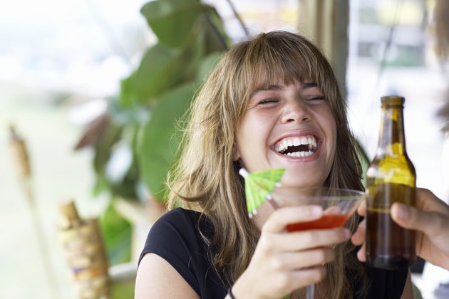 Young woman toasting drink with friend, laughing, close-up