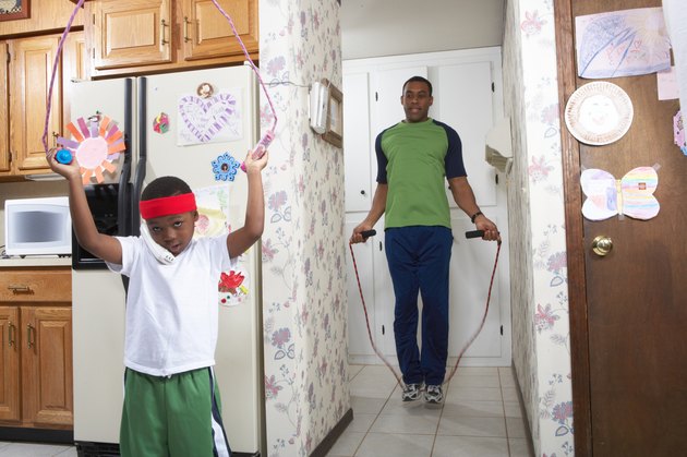 Father and son (4-5) exercising with skipping rope in house