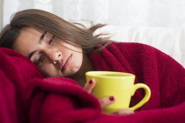 ill young girl with fever drinking cup of warm tea