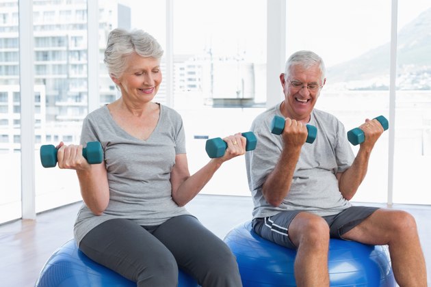 Happy senior couple sitting on fitness balls with dumbbells