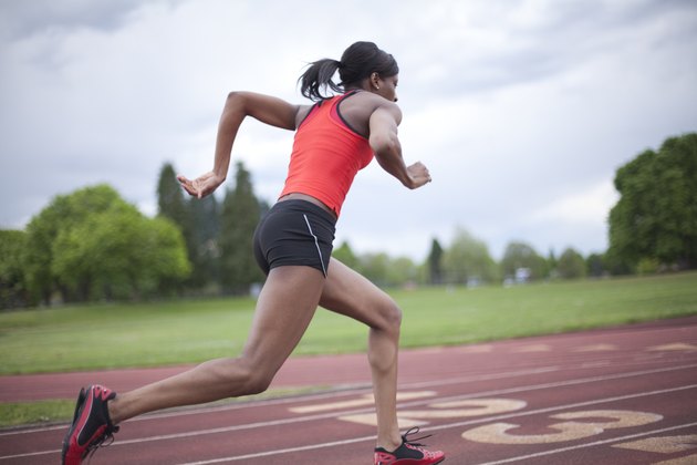 Young female sprinter accelerating, running, side view