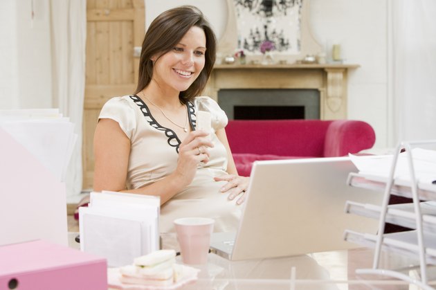 Pregnant woman in home office with laptop eating and smiling