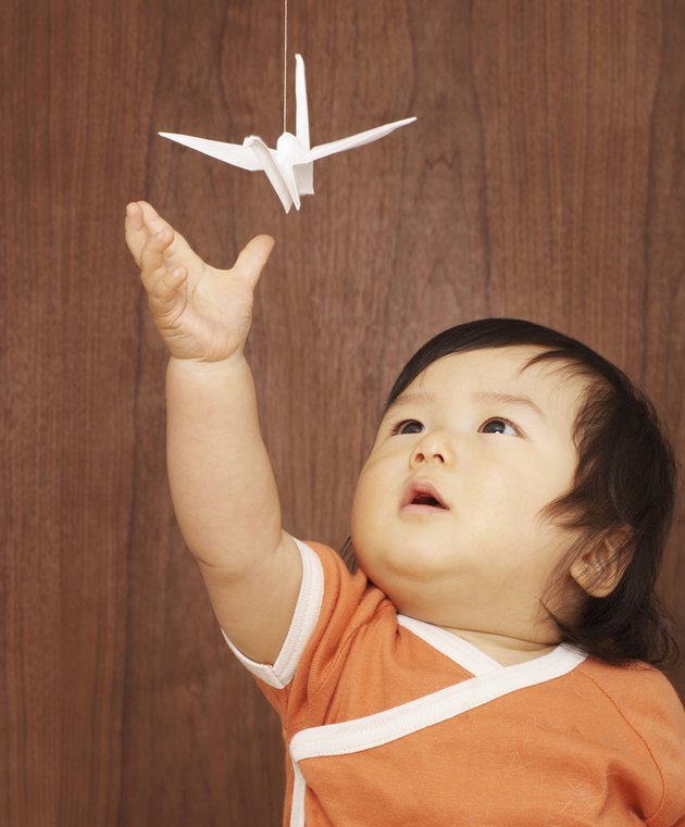 Baby girl (9-12 months) reaching for origami crane hanging from string, close-up