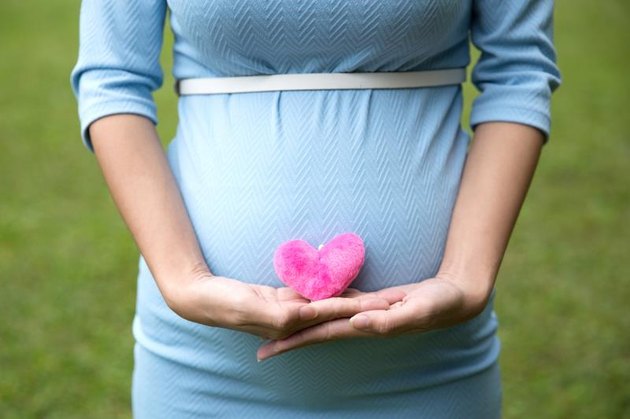 A portrait of a pregnant woman in blue dress holding a single heart shape accessories