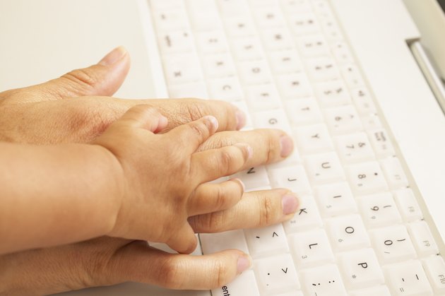 Close-up of a baby's hand holding an adult's hand on a laptop