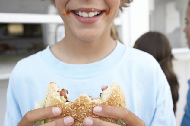 Boy (9-11) holding hamburger with 'bites' missing, smiling, close-up