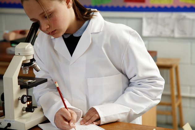 Schoolgirl (11-13) making notes while looking through microscope
