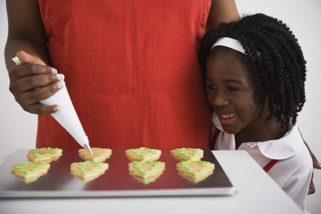 African girl watching mother decorate cookies