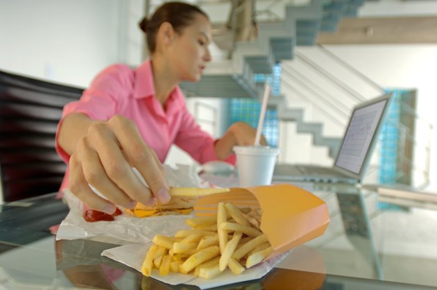 Businesswoman eating French fries, using laptop