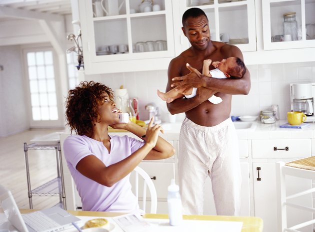 a young woman talking on the phone and a young man standing and holding a baby