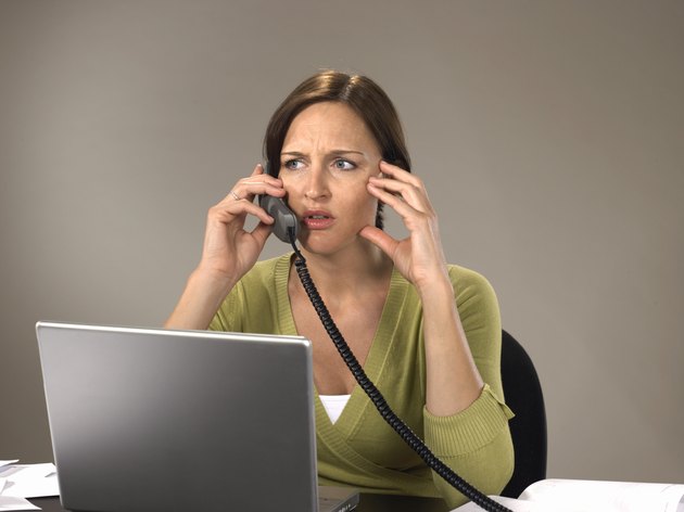 Woman sitting at laptop using telephone, frowning