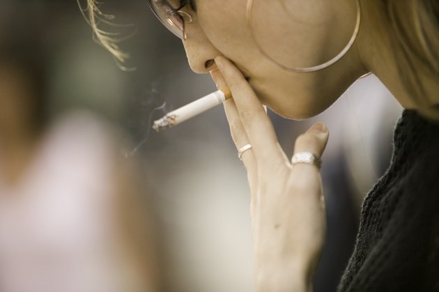 Young woman wearing sunglasses, smoking outdoors, close-up