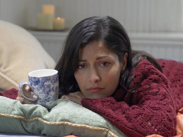 Woman on bed holding cup, resting chin on arm, portrait, close-up