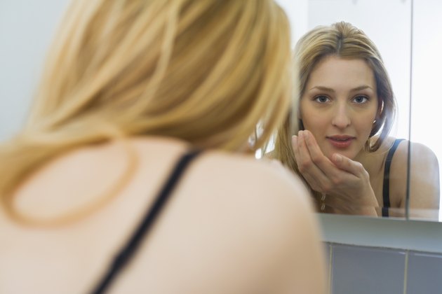 Woman in black bra, looking in bathroom mirror and washing her face