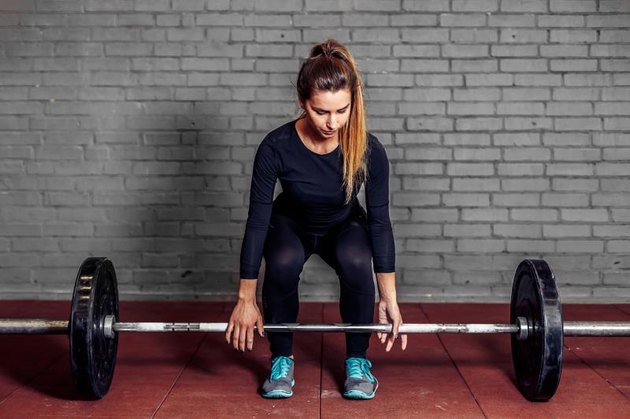 Female athlete doing deadlift at the gym with weight bar. Fitness girl in great shape is lifting weights in a sport gym. Athletic woman train workout.