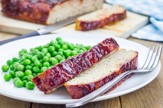 Homemade meatloaf garnished with green peas on a white plate