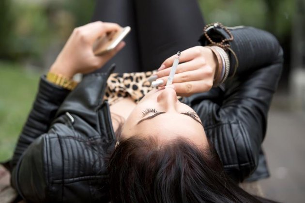 Young woman smoking while relaxing on a bench.