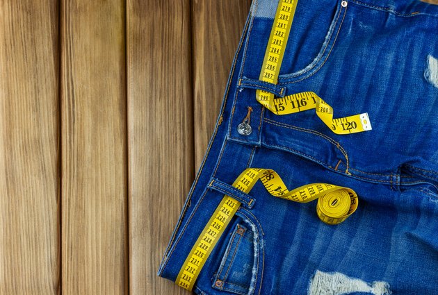 Jeans with measuring tape on wooden background