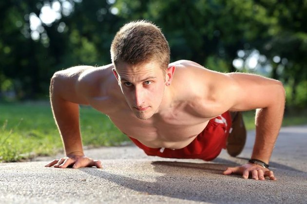 young muscular man push ups on walking road in a park