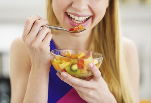 closeup on young woman eating fresh fruits salad in kitchen