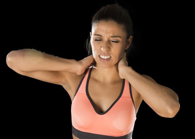 young attractive hispanic fitness woman touching and grabbing her neck and upper back suffering cervical pain isolated on black background in sport injury and body health care concept