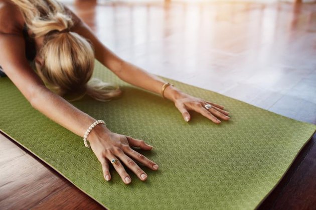 Female doing stretching workout on exercise mat. Woman doing balasana yoga at gym, with focus on hands.