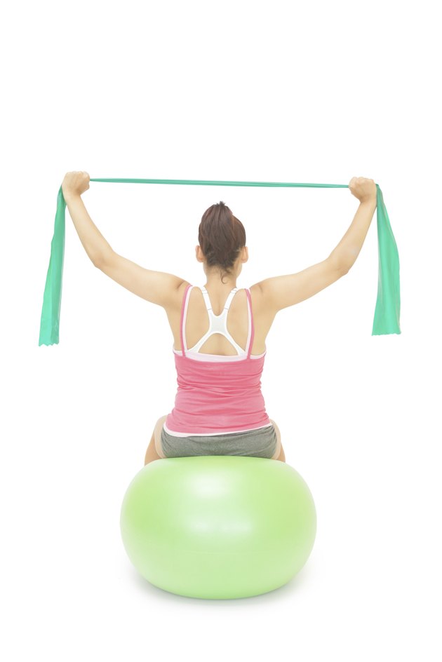 Sporty brunette stretching with resistance band sitting on exercise ball