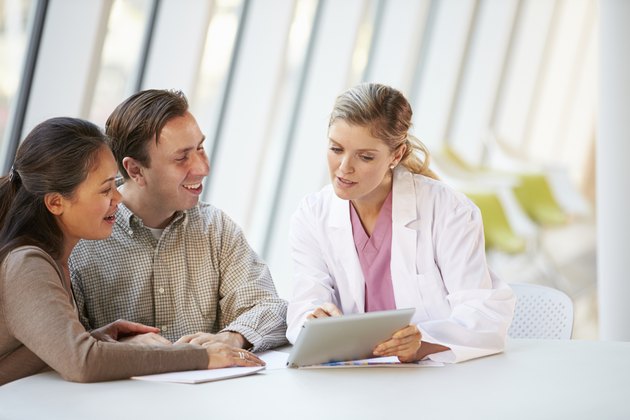 Female Doctor Using Digital Tablet Talking With Patients