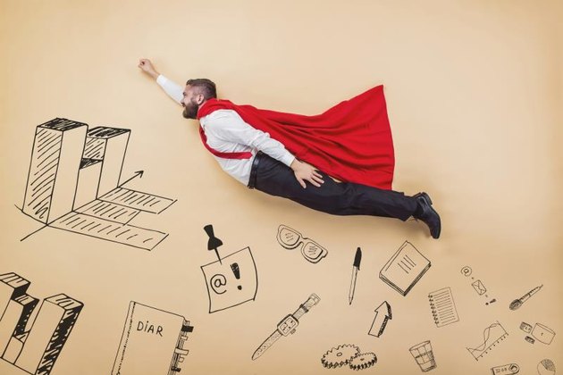 Manager in a superman pose wearing a red cloak. Studio shot on a beige background.