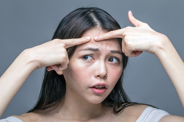 Asian woman squeezing spot on forehead