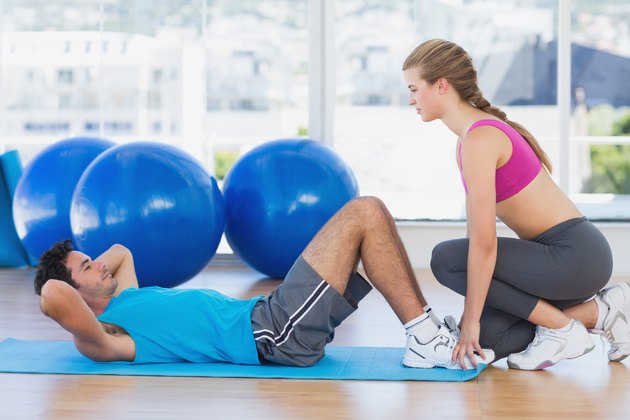 Female trainer helping man with his exercises at gym