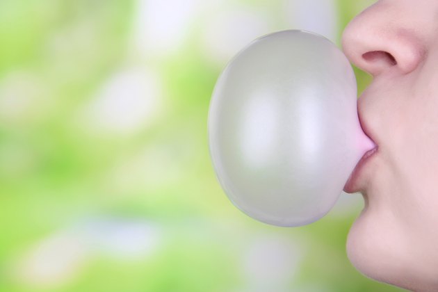 Person doing bubble with chewing gum on bright background
