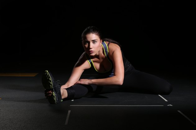 Young woman athlete sitting on the split, black background