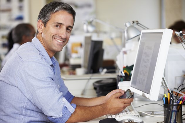 Man Using Mobile Phone At Desk In Busy Creative Office