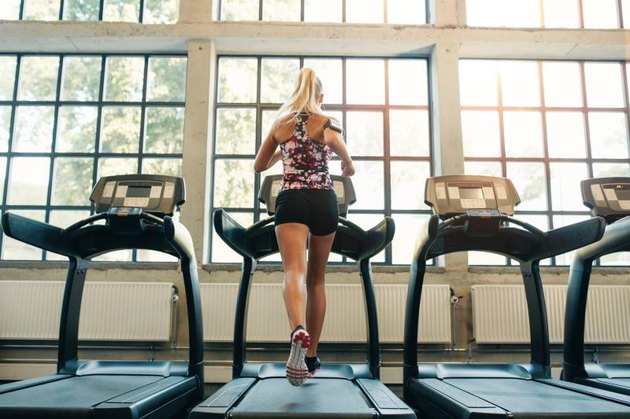 Horizontal shot of woman jogging on treadmill at health club. Female working out at a gym running on a treadmill.